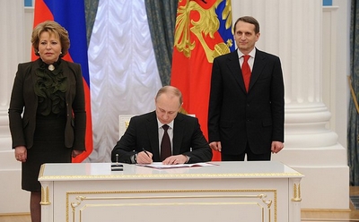 Poetin, gezeten achter een bureau, tekent wetsdocumenten