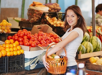 lachend meisje voor een fruitkraam met een mandje ter hoogte van haar middel