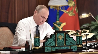 vr de ceremonie zit Poetin in hemdsmouwen achter zijn bureau